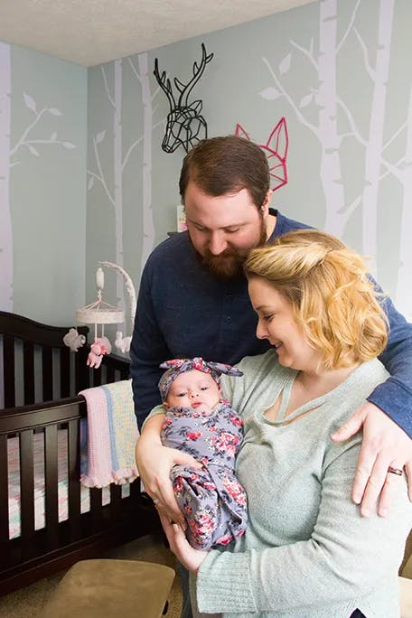 New family of three - parents looking down at their newborn in their nursery
